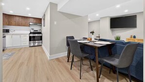 Een moderne keuken met ingebouwde apparatuur, een eethoek met een tafel en stoelen, en een zithoek met een bank en een flatscreen-televisie.