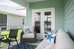 A covered porch with a wicker chair, a small table, and a sofa with starfish pillows. - NEW! 5BR WindMark | Golf Cart | Pet Friendly (Port St. Joe)