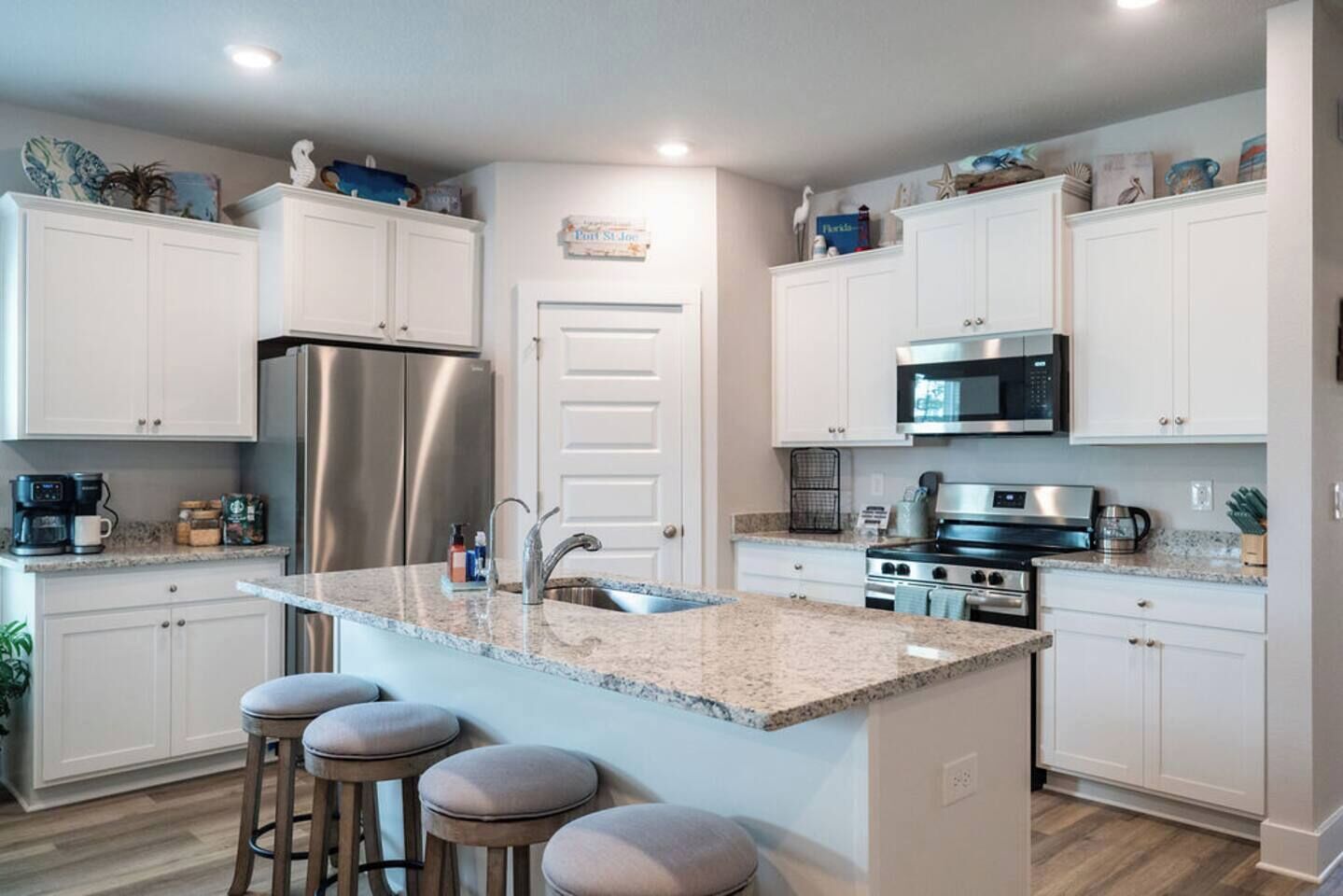 A modern kitchen with white cabinets, stainless steel appliances, a granite countertop, and a central island with bar stools.