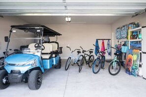 A garage with a blue golf cart, bicycles, and a surfboard rack. - NEW! 5BR WindMark | Golf Cart | Pet Friendly (Port St. Joe)