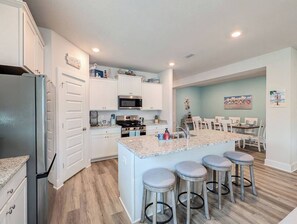 A modern kitchen with white cabinetry, a central island with bar stools, and a dining area with a table and chairs.