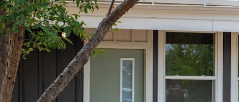 A house with a front door, a small porch, two potted plants, and a tree.