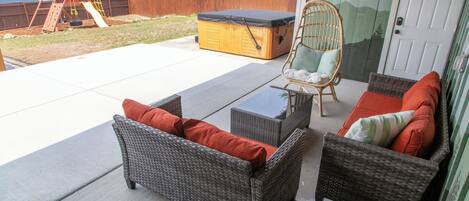 An outdoor patio with wicker furniture, a swing set, and a hot tub.