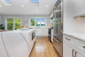 A modern kitchen with white cabinetry, a large island, stainless steel appliances, and a view of greenery outside.