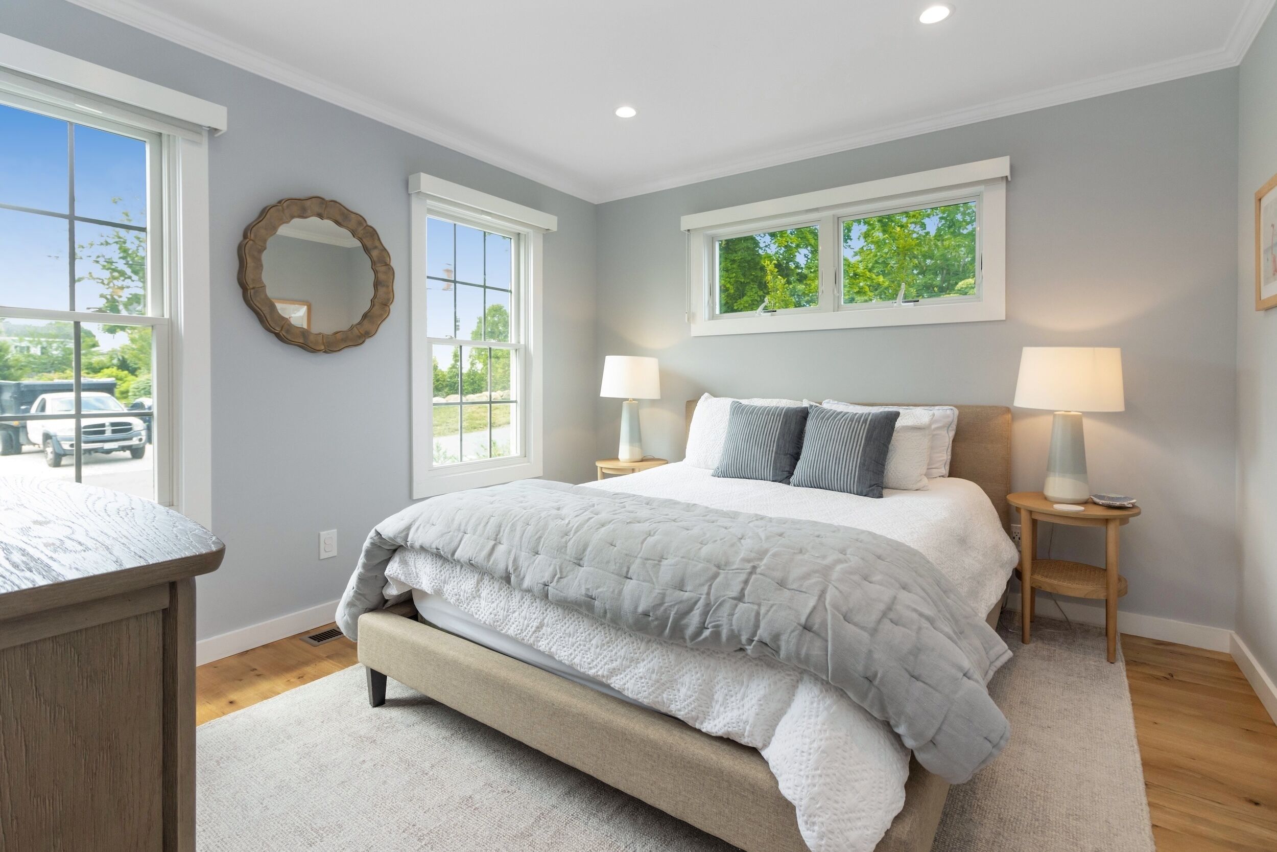 A bedroom with a bed, two bedside tables, a mirror, and windows.
