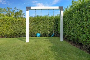 Un jardín con un columpio blanco y una cesta azul.