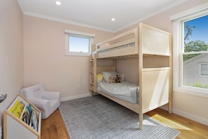Ein Schlafraum mit Etagenbett, Fenster, kleinem Stuhl und Bücherregal.