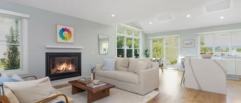 A living room with a fireplace, a sofa, a coffee table, and a view of the kitchen.