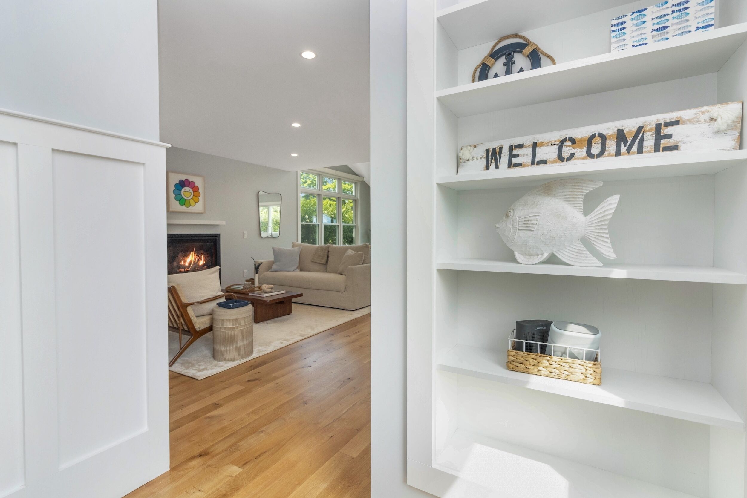 A modern living room with a fireplace, a sofa, and a coffee table. There are shelves with decorative items and a 'WELCOME' sign.