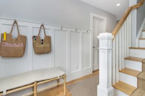 A hallway with a bench, a staircase, and two woven baskets hanging on the wall.