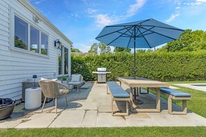 A patio with a table, chairs, a bench, and an umbrella. - 5BR family luxury retreat w/ AC, pool in Greenport. Chef's kitchen, private yard (Greenport)