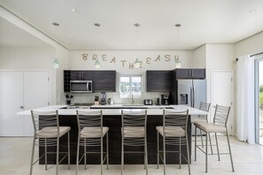 A modern kitchen with a central island, bar stools, dark cabinetry, and a 'BREATHE EASY' sign. - Modern Canal-front Villa in Leeward (Leeward Settlement)