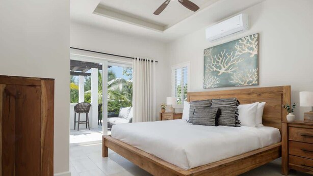 Ein Schlafzimmer mit einem hölzernen Bett, einem Deckenventilator, einem Gemälde und Blick ins Freie.