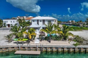 A beachfront property with a pool, palm trees, and a dock. - Modern Canal-front Villa in Leeward (Leeward Settlement)