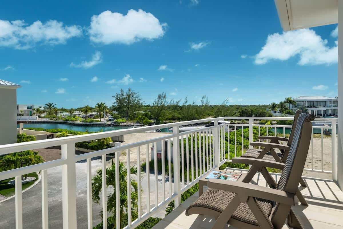 A balcony with a view of a swimming pool and a beach, surrounded by greenery.
