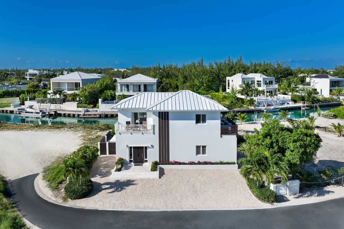 Una casa moderna de dos pisos con balcón, rodeada por una piscina y una playa.