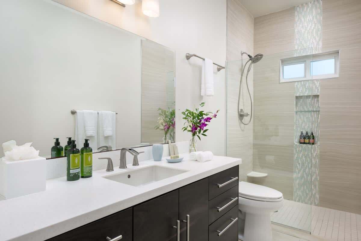 A modern bathroom with a large mirror, dual sinks, a toilet, and a shower area.