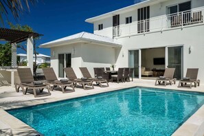 Un espace aménagé au bord de la piscine, avec des chaises longues et un bâtiment doté d’un balcon.