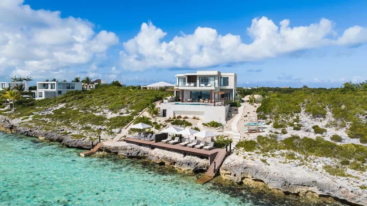A modern beachfront property with a pool, lounge chairs, and a view of the ocean.