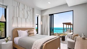 Ein modernes Schlafzimmer mit einem großen Bett, Meerblick und einem Balkon mit Gartenmöbeln.