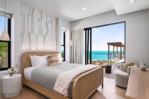Ein modernes Schlafzimmer mit einem großen Bett, Meerblick und einem Balkon mit Gartenmöbeln.