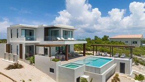 Ein modernes, zweistöckiges Haus mit Schwimmbad, Sitzgelegenheiten im Freien und Blick auf die umliegende Landschaft.