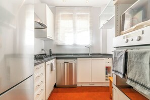 Eine kleine Küche mit Geschirrspüler, Backofen und einem Fenster über der Spüle.