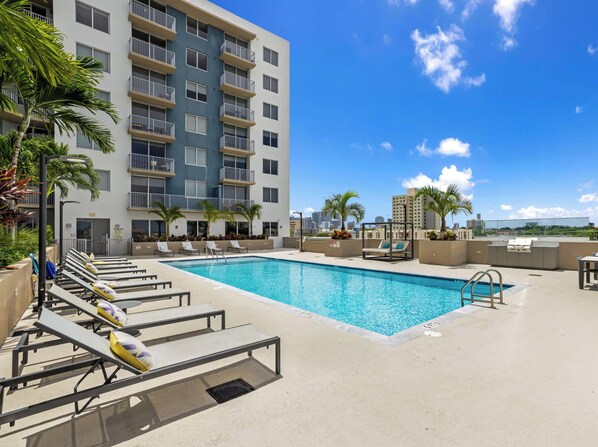 A rooftop pool area with lounge chairs, a pool, and a building with balconies.
