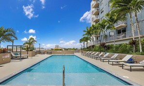A swimming pool with lounge chairs and palm trees, surrounded by a building with balconies. - Sleek Miami 2BR | Free parking | Pool & Gym (Miami)