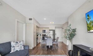 A modern kitchen with a dining area, a gray sofa, and a potted plant.