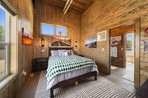 A wooden room with a bed, two windows, and a door.