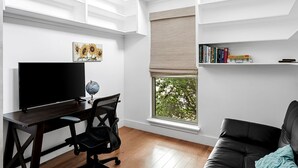 A modern living room with a flat-screen TV, a desk, and a bookshelf.