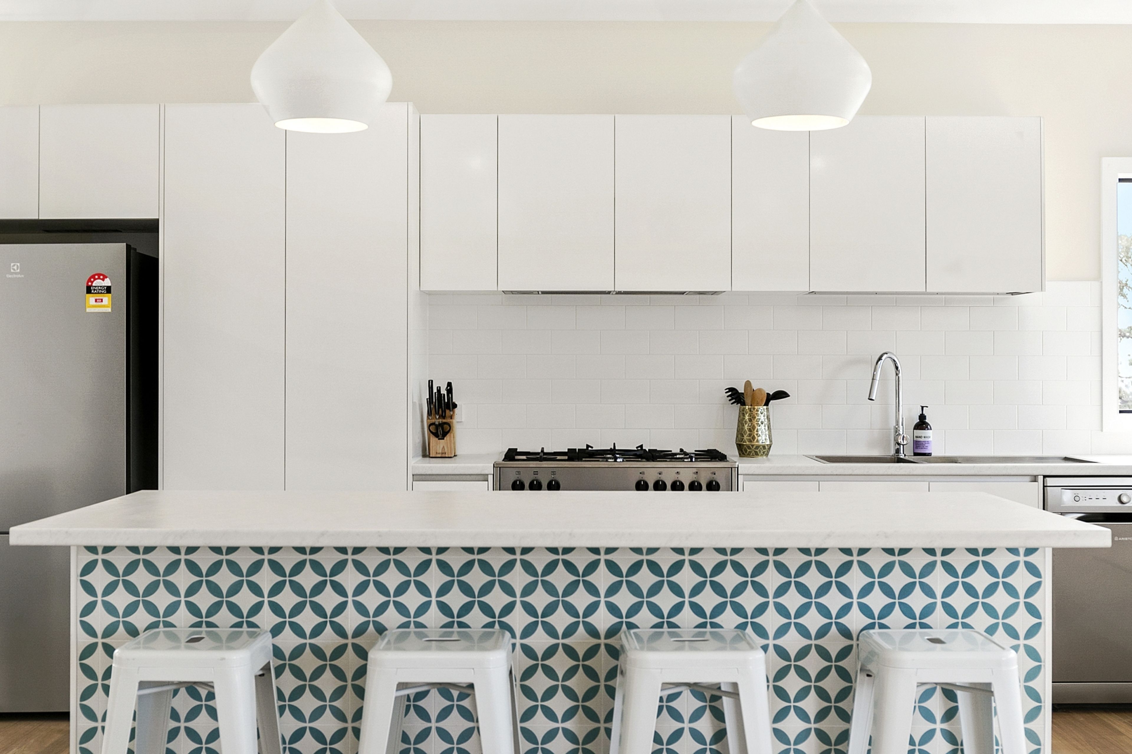 A modern kitchen with white cabinets, a central island with stools, a gas stove, and pendant lighting.