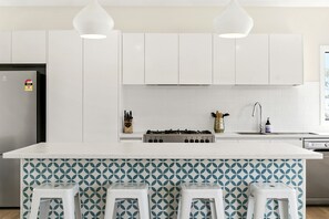 A modern kitchen with white cabinets, a central island with stools, a gas stove, and pendant lighting. - Vue Sur La Mer - Pour Deux Ocean view for two (Wye River)