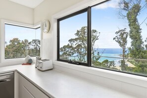 A kitchen with a large window overlooking a beach and trees. - Vue Sur La Mer - Pour Deux Ocean view for two (Wye River)
