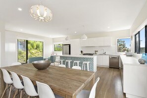 A modern kitchen with white cabinetry, a wooden dining table, and a large window. - Vue Sur La Mer - Pour Deux Ocean view for two (Wye River)