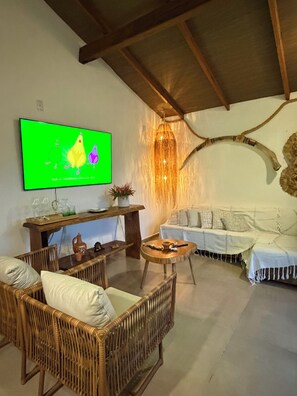A living room with a television, wicker furniture, a wooden coffee table, and a white sofa. - Humpback Whale House Azul (Caraíva)