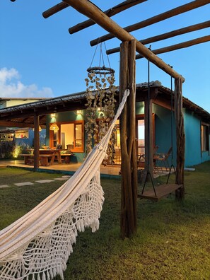 A hammock, wooden swing, and a building with a patio. - Humpback Whale House Azul (Caraíva)