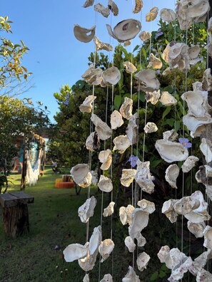A garden with hanging shells and a wooden bench. - Humpback Whale House Azul (Caraíva)