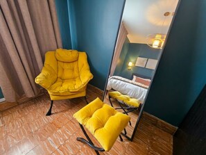 A room with a mirrored wall, a yellow armchair, a yellow ottoman, and a bed with white bedding. - SJ City Oasis Pool Billiards Power & Water Back up (San Juan)