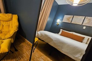 Ein Zimmer mit einem Bett, einem gelben Sessel, einer Wandleuchte und drei Wandbildern.