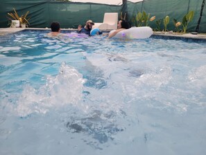 Une piscine avec des personnes dans l’eau, dont certaines utilisent des bouées gonflables.