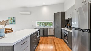 A modern kitchen with a central island, stainless steel appliances, and a window providing a view of greenery. - Fairhaven Treetops Lookout (Fairhaven)