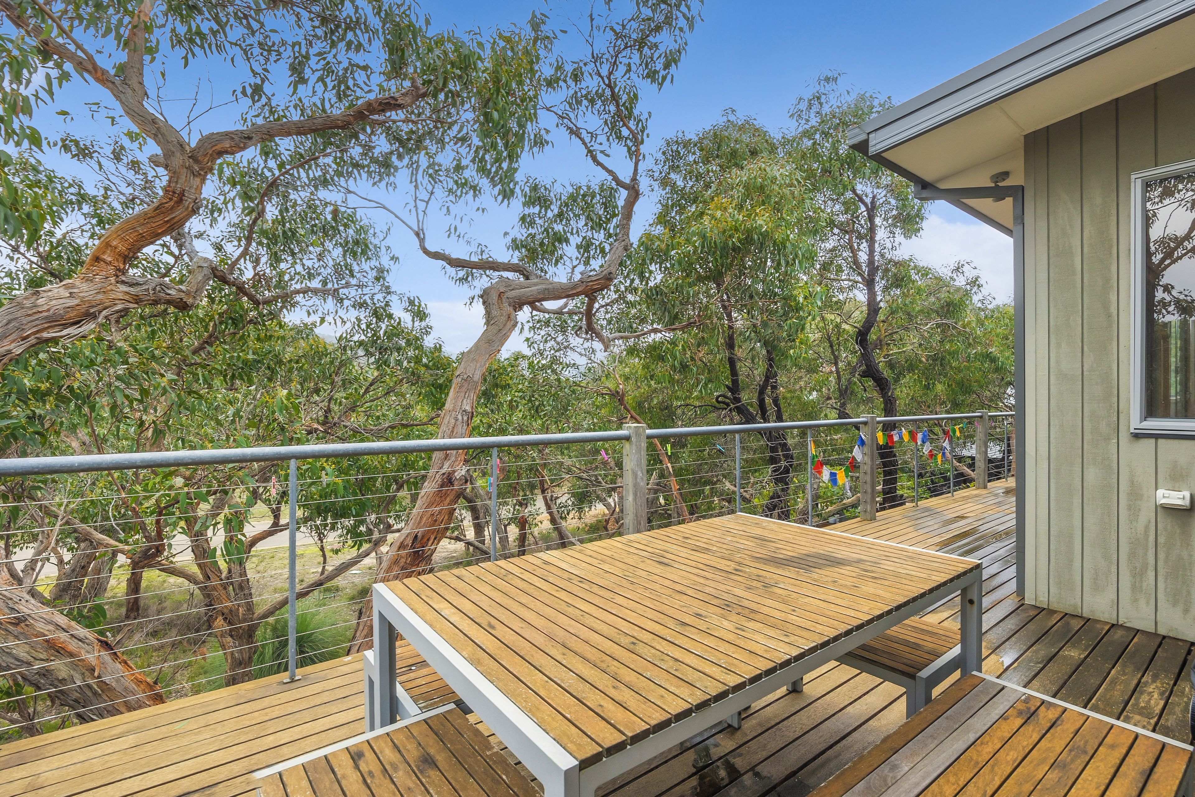A wooden deck with a metal railing, overlooking a natural landscape with trees and a clear sky.