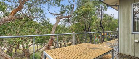 A wooden deck with a metal railing, overlooking a natural landscape with trees and a clear sky.