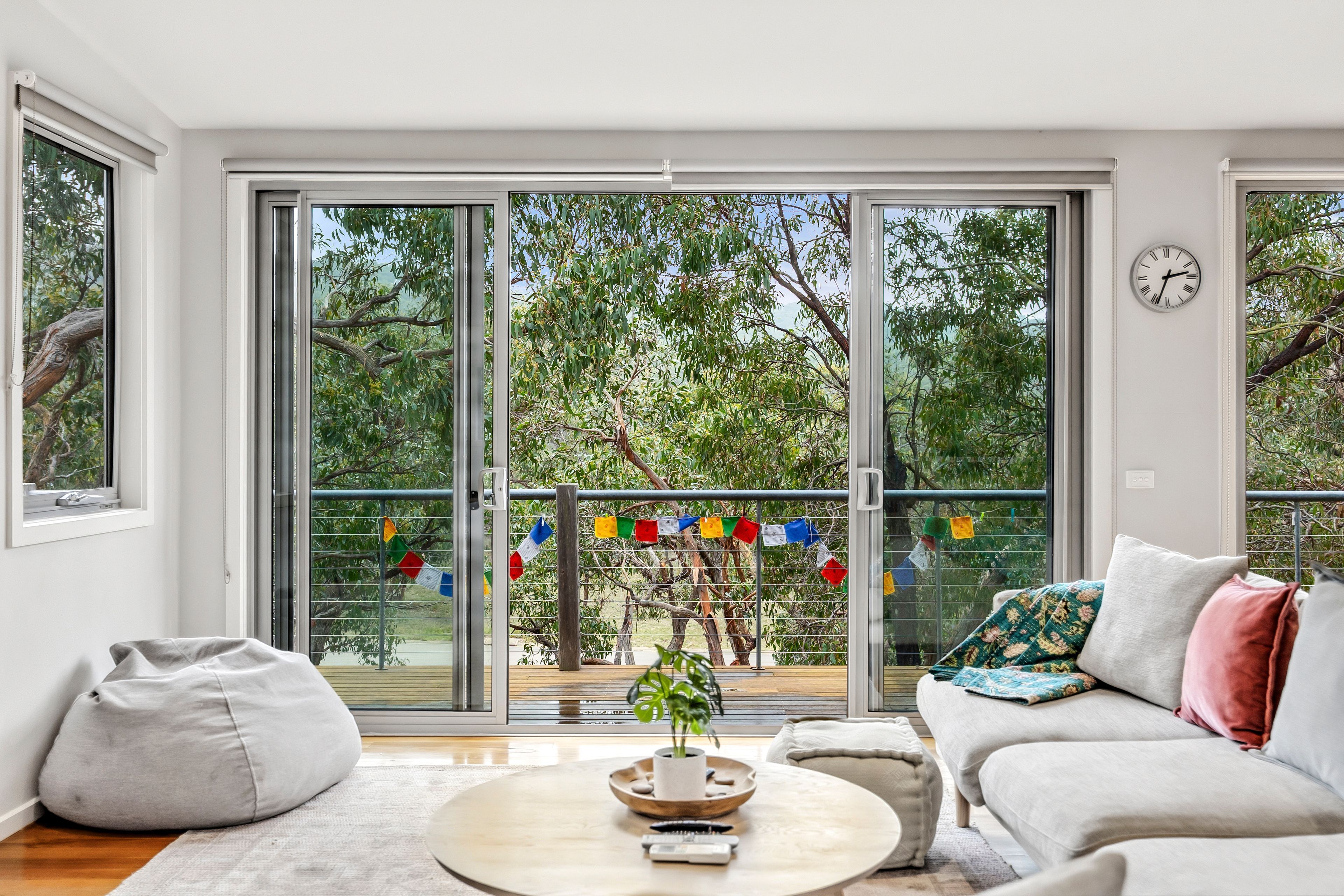 A modern living room with a sliding glass door leading to a balcony, a round coffee table, and a sofa with cushions.