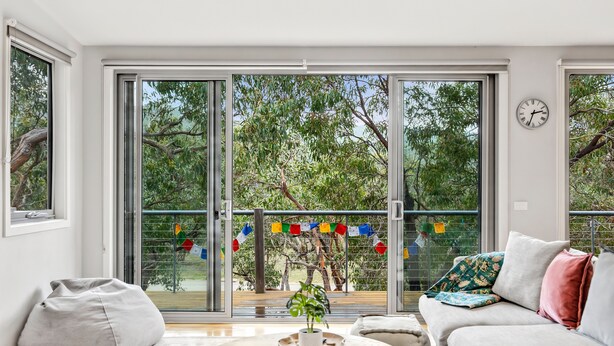 A modern living room with a sliding glass door leading to a balcony, a round coffee table, and a sofa with cushions. - Fairhaven Treetops Lookout (Fairhaven)