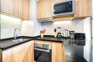 A modern kitchen with wooden cabinets, a stainless steel oven, a microwave, and a coffee maker. - Estoril Suite | Clínica y Centro Comercial (Las Condes)