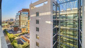 Un edificio moderno de varios pisos, con grandes ventanales y un estacionamiento con algunos vehículos.