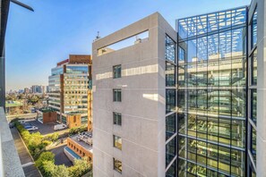 A modern building with multiple floors, large windows, and a parking area with a few vehicles. - Estoril Suite | Clínica y Centro Comercial (Las Condes)